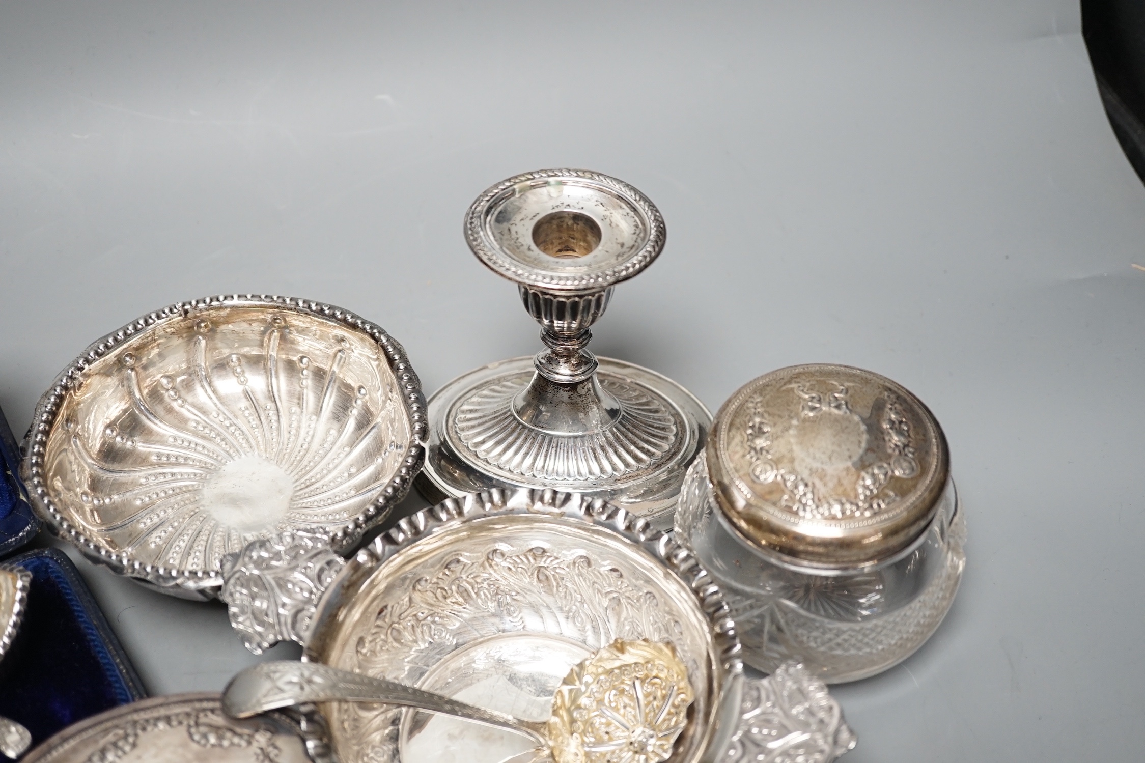 A Victorian repousse silver two handed bowl, one other silver bowl, a silver sifter spoon, four silver mounted glass toilet jars, a silver dwarf candlestick and a cased pair of silver salts.